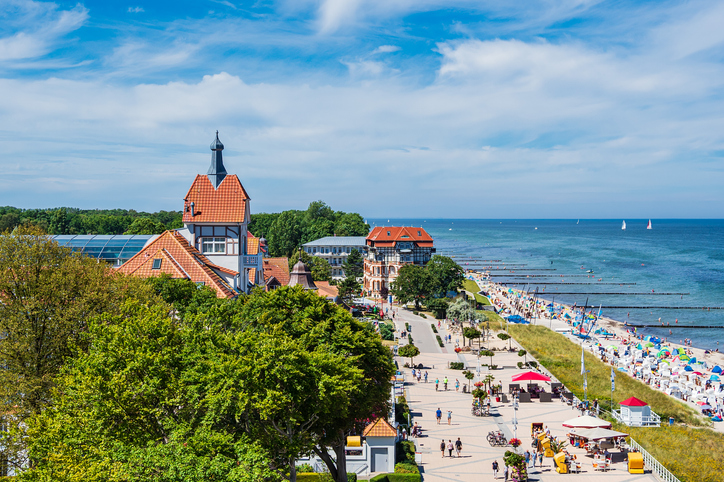 Strand von Kühlungsborn mit Promenade, Strandkörben und Spaziergängern bei Sonnenschein.