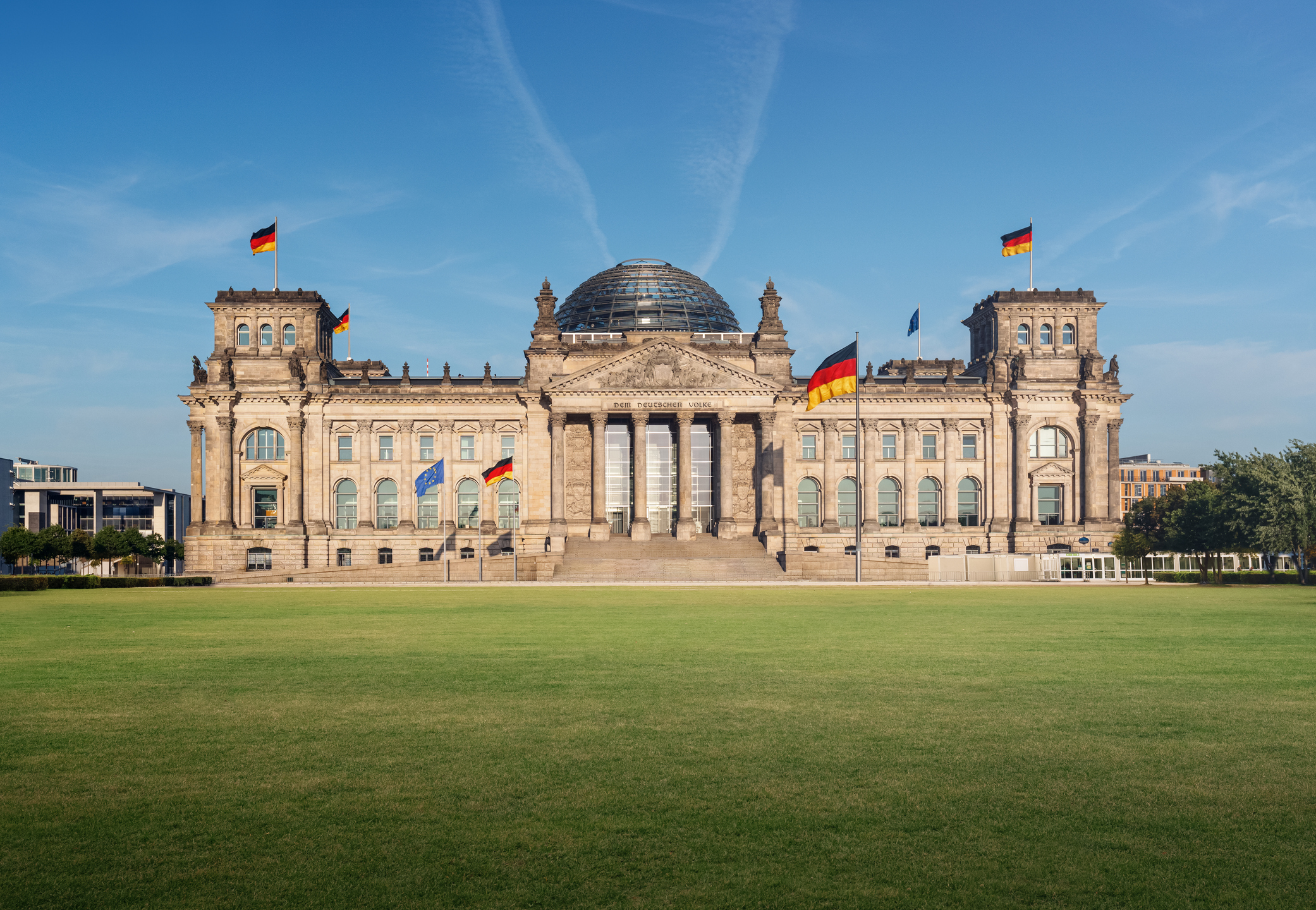 Reichstagsgebäude in Berlin bei Tageslicht, frontal mit weitläufigem Rasenplatz im Vordergrund.