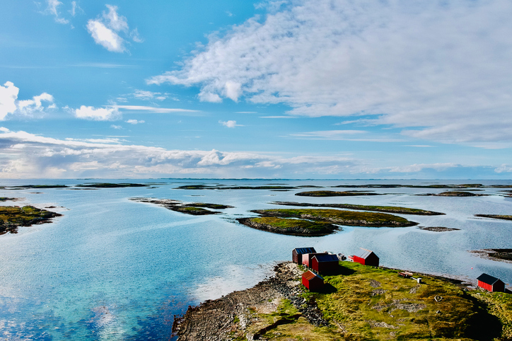 Kleine rote Holzhäuser am Ufer der Insel Vega in Norwegen, umgeben von Meer und Inseln.