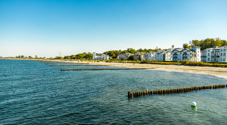 Blick auf den Ostseestrand von Heiligendamm mit Seebad-Villen und Buhnen im Wasser.