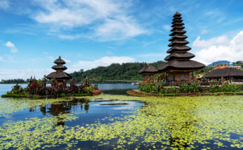 Pura Ulun Danu Bratan Wassertempel auf Bali, im Vordergrund schwimmende Seerosen auf dem See.