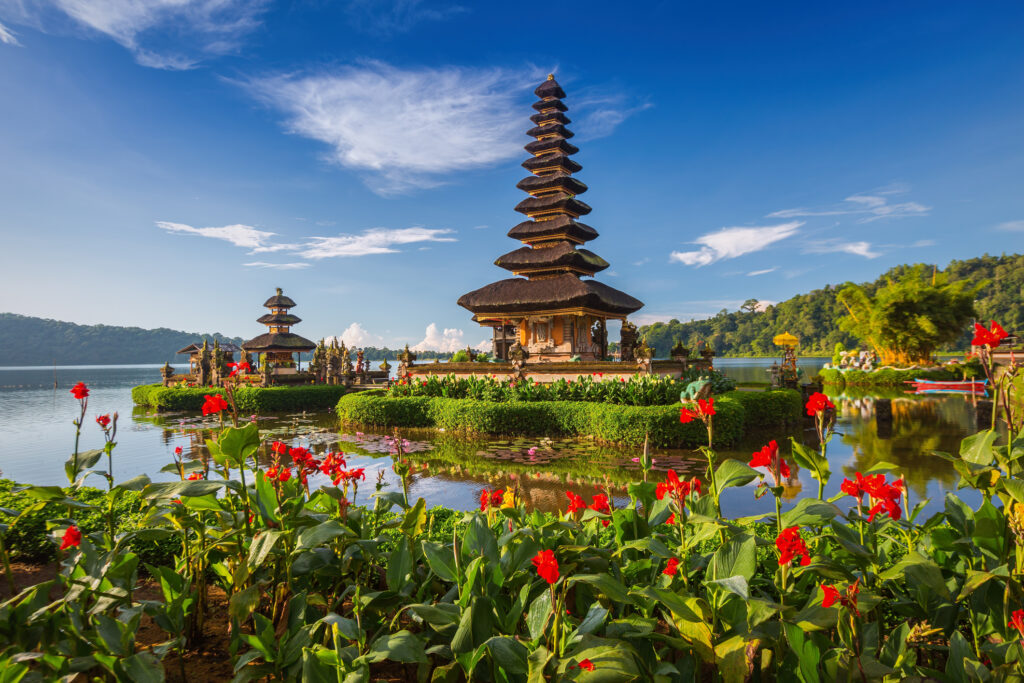 Pura Ulun Danu Bratan auf Bali, Wassertempel am See mit farbenfrohen Blumen im Vordergrund.