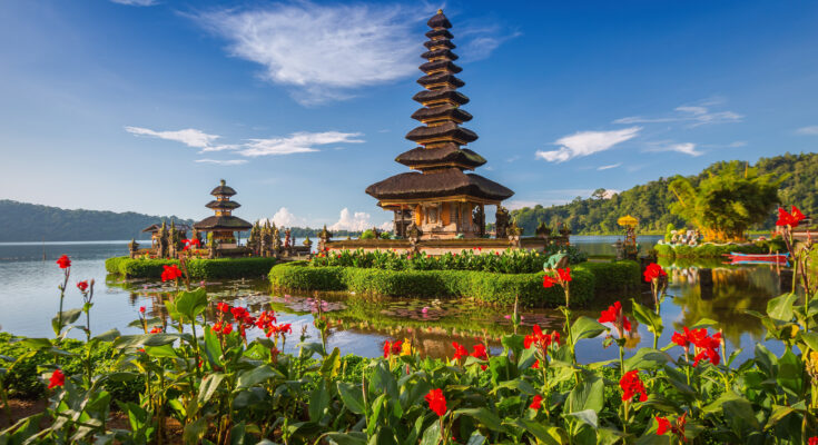 Pura Ulun Danu Bratan auf Bali, Wassertempel am See mit farbenfrohen Blumen im Vordergrund.