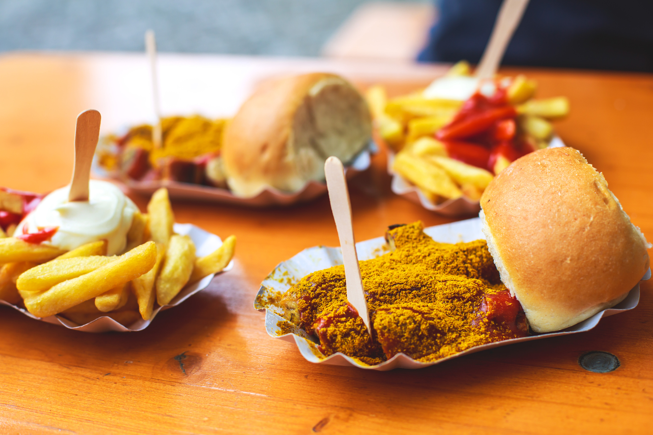 Currywurst mit Pommes und Brötchen auf Pappteller, typisch Berliner Imbissgericht.