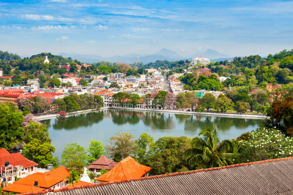 Blick auf den Kandy-See, umgeben von Gebäuden, Bäumen und Bergen im Hintergrund.