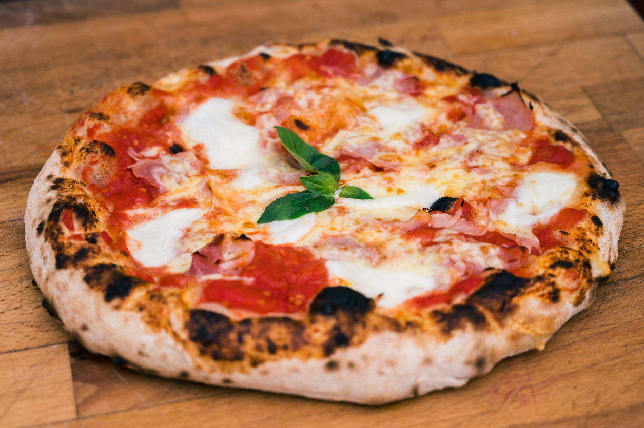 Frische Pizza Napoletana mit Tomatensauce, Mozzarella, Schinken und Basilikum auf einem Holzbrett.