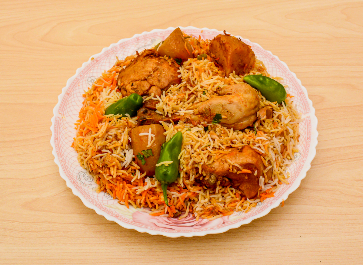 Nahaufnahme eines Tellers Chicken Biryani, zubereitet mit aromatischem Basmatireis, Hühnerstücken, Kartoffeln und grünen Chilischoten, serviert auf einem dekorativen Porzellanteller.