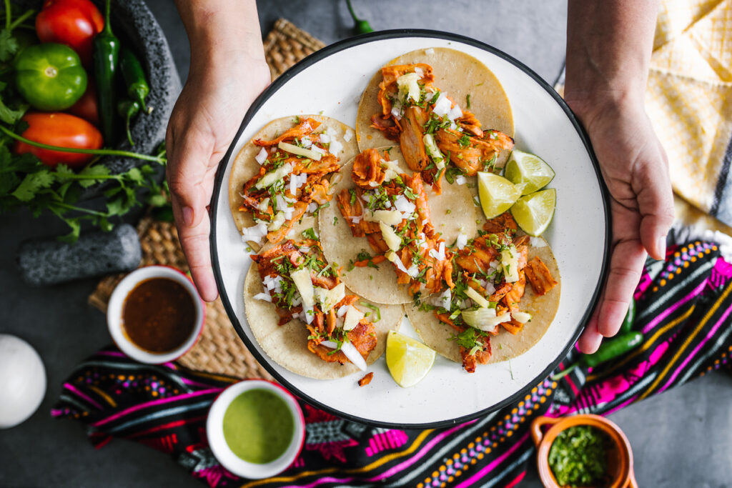 Nahaufnahme von Tacos al Pastor auf einem Teller, garniert mit Ananas, Zwiebeln, Koriander und Limettenstücken.