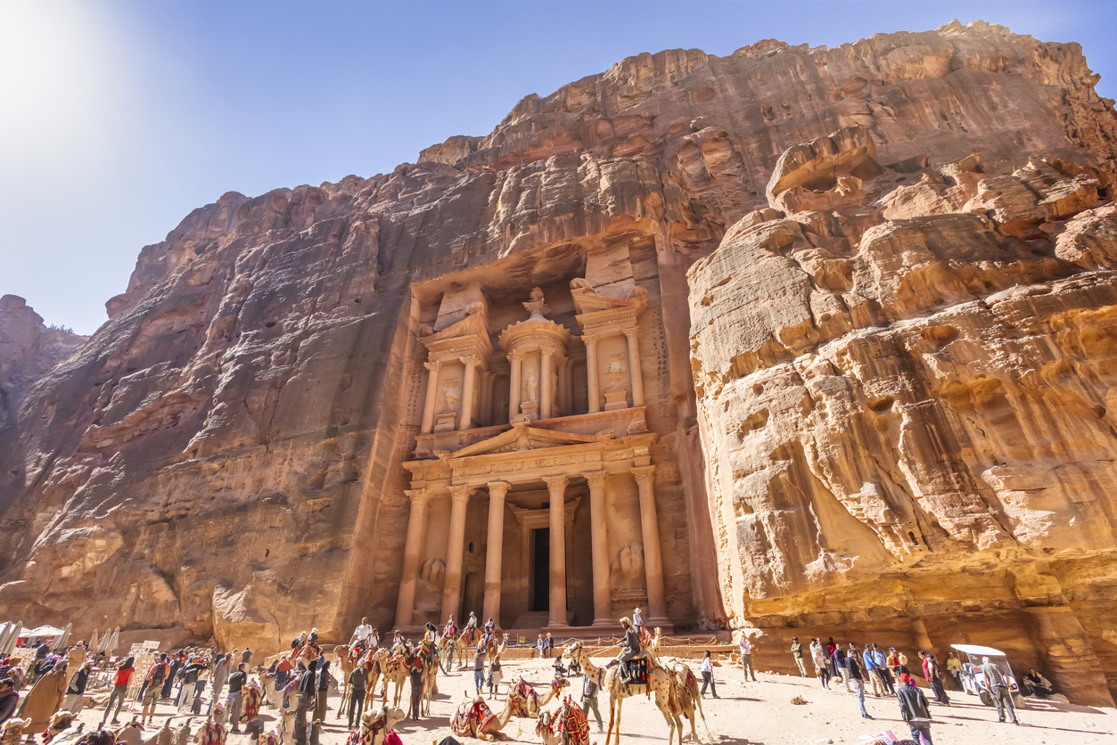 Das Schatzhaus von Petra in Jordanien, in den rötlichen Fels gehauen, mit Touristen und Kamelen im Vordergrund.