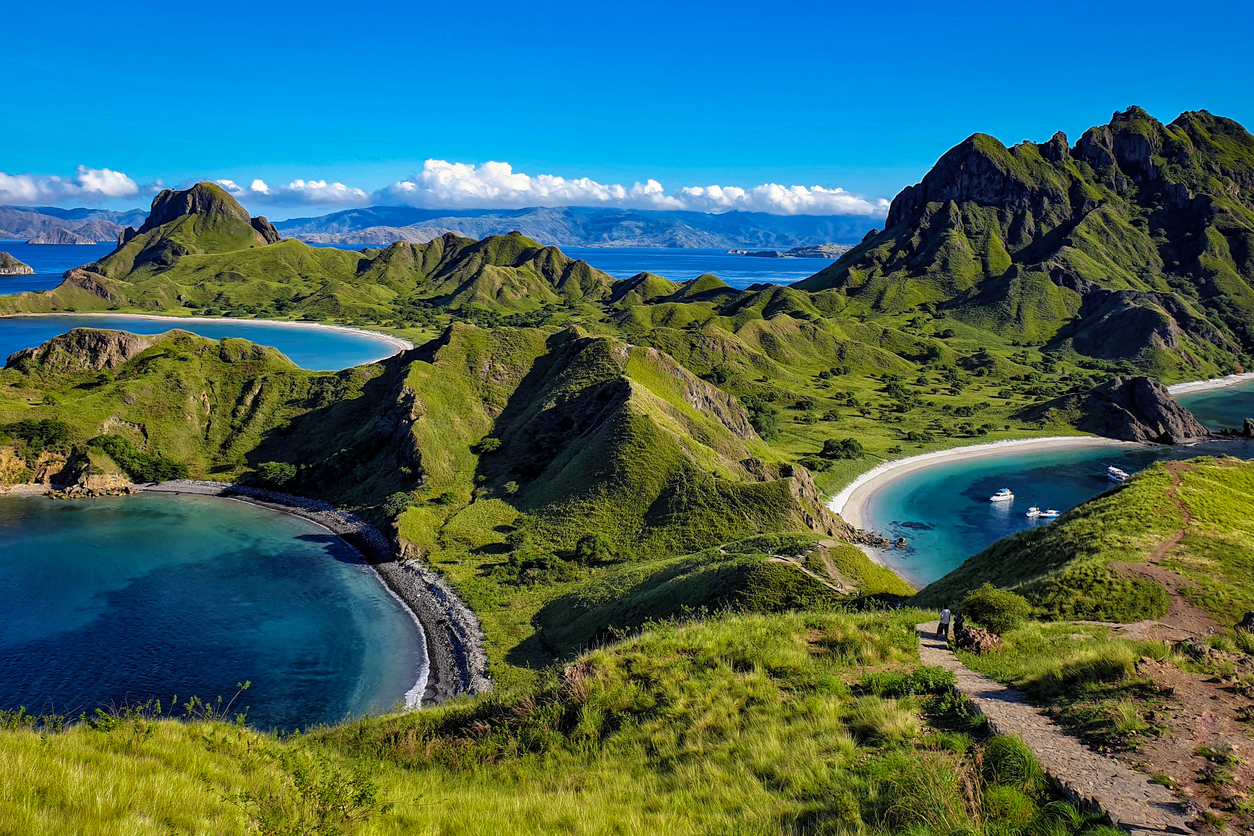 Blick auf die grünen Hügel und Buchten des Komodo-Nationalparks mit weißen Sandstränden und türkisfarbenem Wasser.