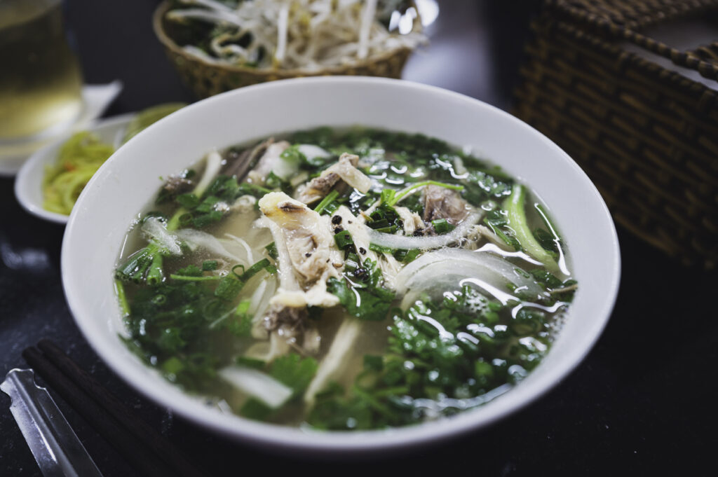 Schüssel mit Phở Gà, einer vietnamesischen Hühnersuppe mit Reisnudeln, Kräutern und Zwiebeln.