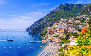 Luftaufnahme von Positano an der Amalfiküste in Italien mit bunten Häusern, Strand, Sonnenschirmen und Booten im türkisblauen Mittelmeer.