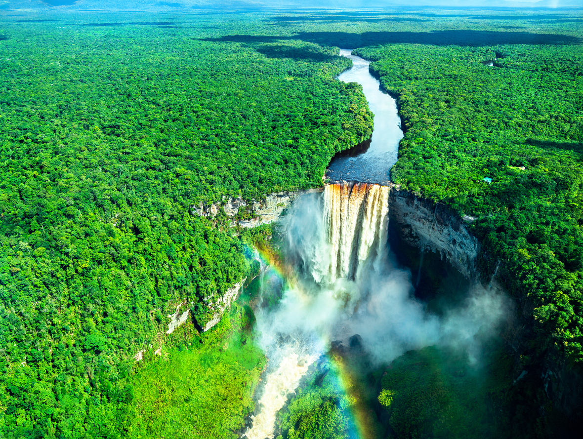 Luftaufnahme der Kaieteur Falls in Guyana, umgeben von dichtem tropischen Regenwald, mit Regenbogen im aufsprühenden Wassernebel.