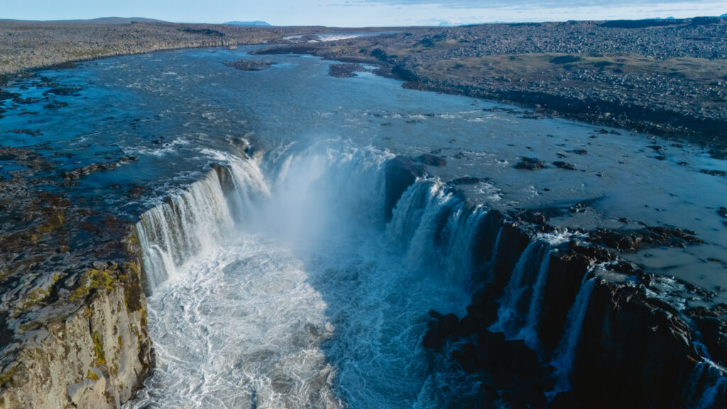 Drohnenaufnahme des Dettifoss-Wasserfalls in Island, bei dem gewaltige Wassermassen in eine tiefe Schlucht stürzen, umgeben von karger, vulkanischer Landschaft.
