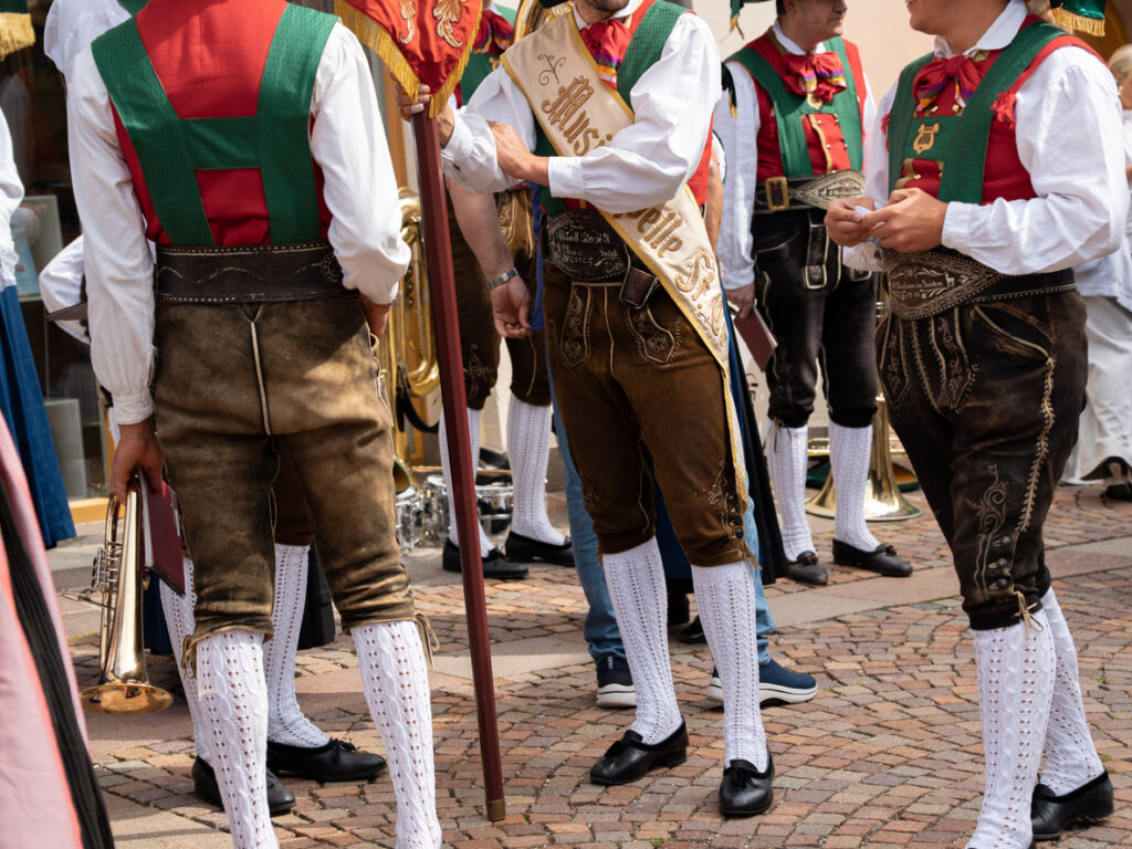 Männer in traditioneller Südtiroler Tracht mit Lederhosen, weißen Kniestrümpfen und farbigen Westen bei einer Blaskapelle.