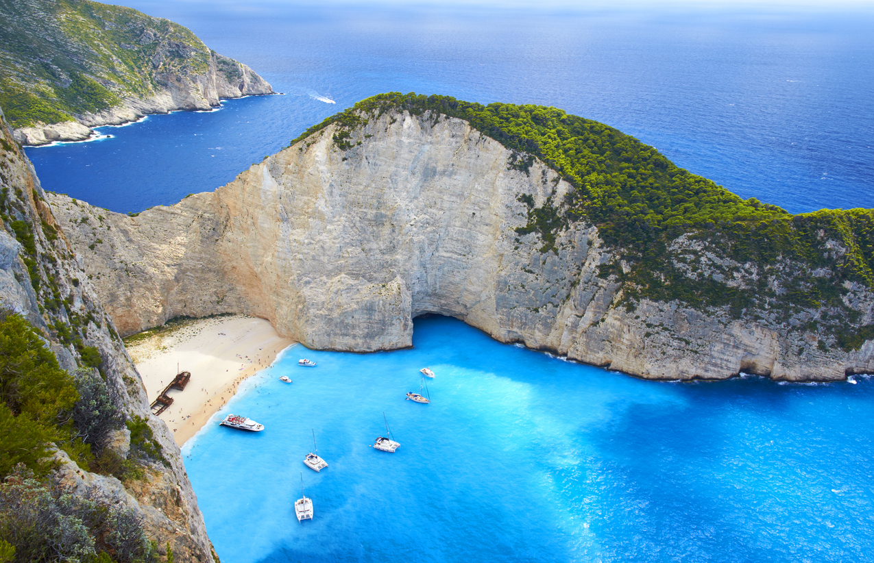 Atemberaubende Luftaufnahme des Navagio Beach auf Zakynthos, Griechenland, mit weißem Sandstrand, türkisblauem Wasser, hohen Klippen und dem berühmten Schiffswrack, umgeben von Booten im klaren Meer.
