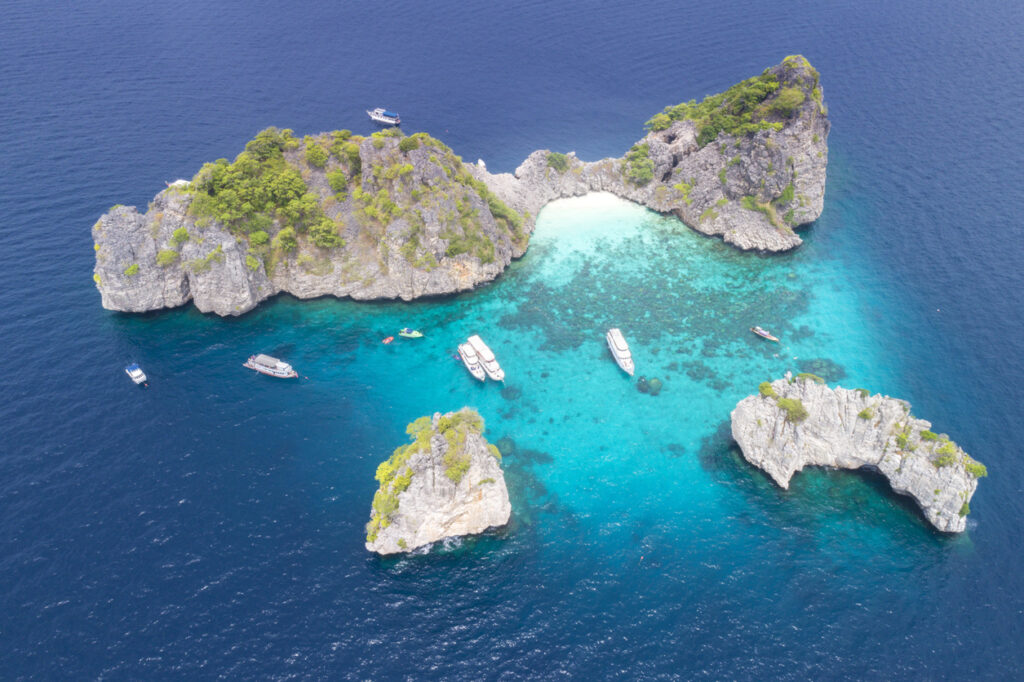 Luftaufnahme der Koh Ha Inseln bei Koh Lanta in Thailand mit kristallklarem türkisfarbenem Wasser, weißen Stränden und Booten im Meer.