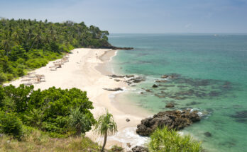 Tropischer Sandstrand auf Koh Lanta in Thailand mit grünem Dschungel, türkisfarbenem Wasser und Felsen am Ufer.
