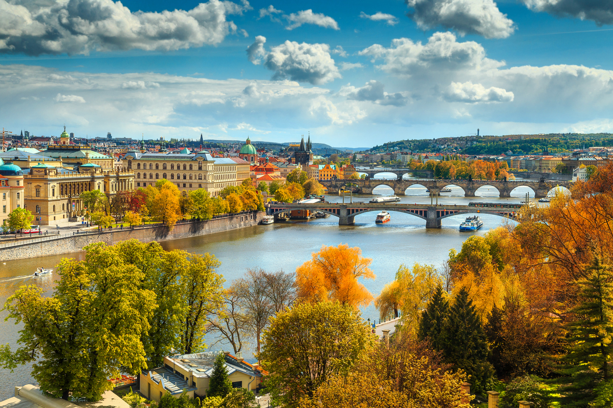 Herbstlicher Panorama-Blick auf Prag mit Moldau, mehreren Brücken und farbigem Laub.