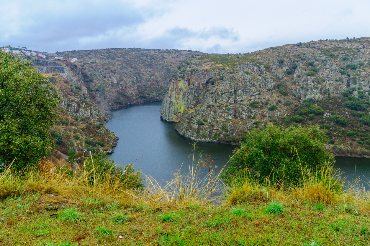 Flussschlucht bei Miranda do Douro mit Felswänden, Flussschleife, Gras im Vordergrund und Wolkenhimmel.