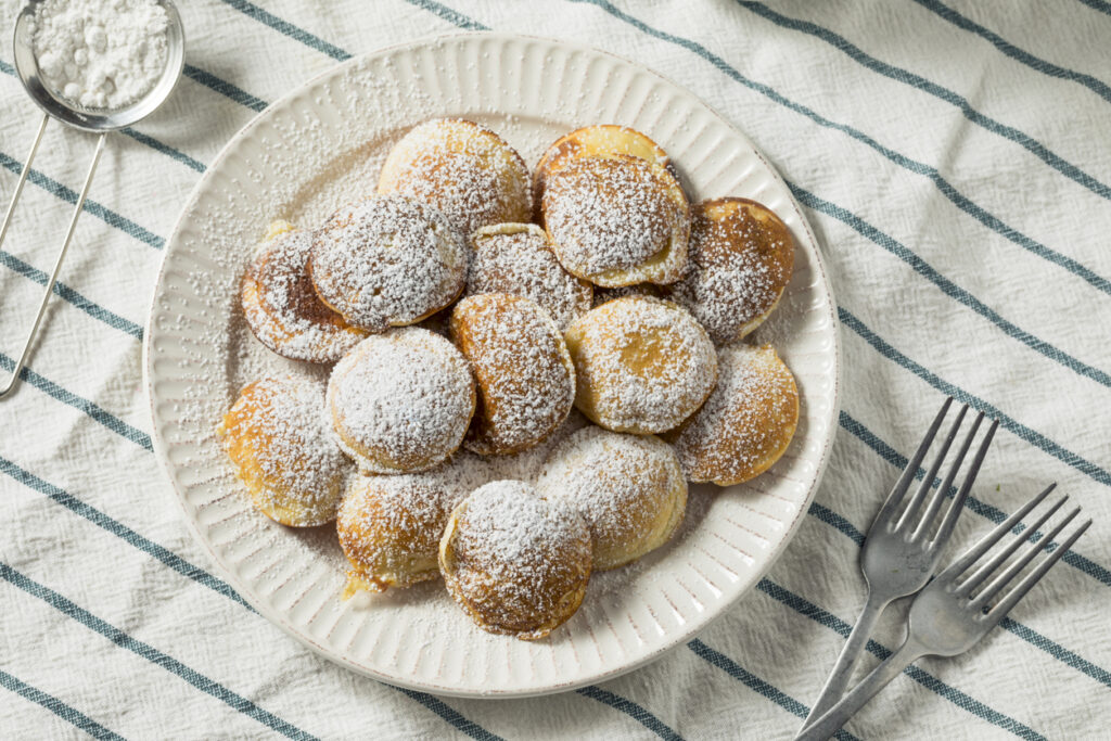 Niederländische Poffertjes, kleine fluffige Pfannkuchen, auf einem Teller angerichtet und mit Puderzucker bestäubt.