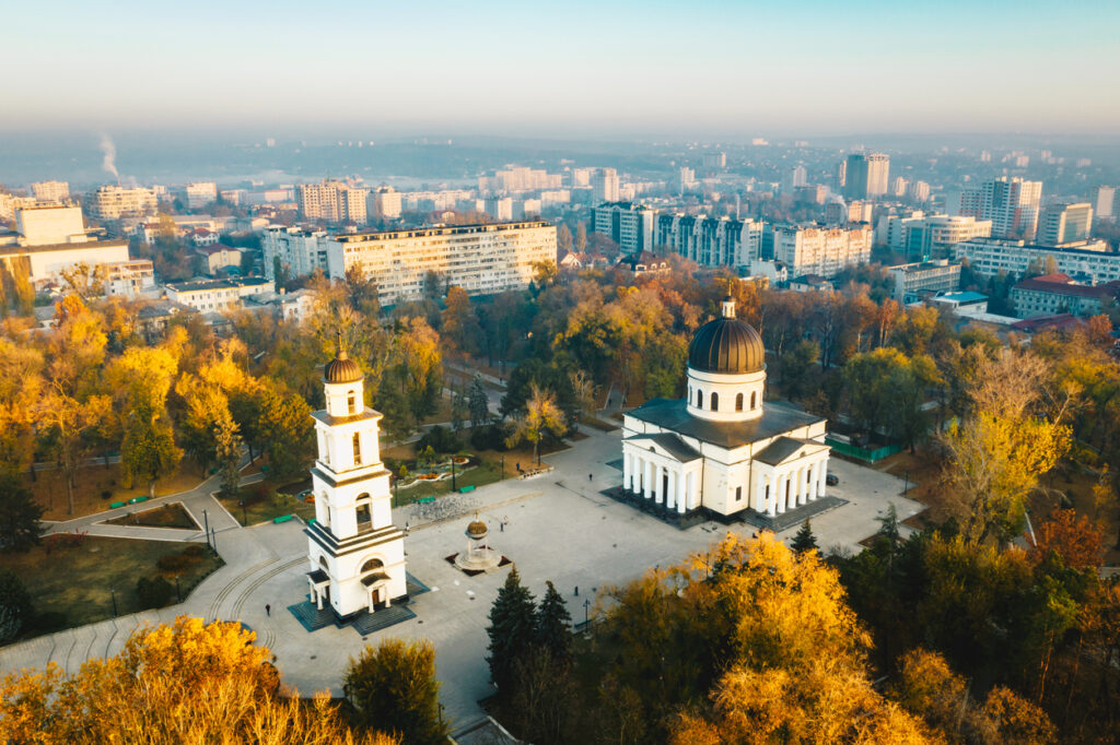 Drohnenaufnahme des Kathedralparks in Chișinău mit der weiß-klassizistischen Kathedrale mit schwarzer Kuppel und freistehendem Glockenturm, umgeben von herbstlichen Bäumen und Stadtbebauung.