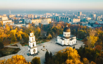 Drohnenaufnahme des Kathedralparks in Chișinău mit der weiß-klassizistischen Kathedrale mit schwarzer Kuppel und freistehendem Glockenturm, umgeben von herbstlichen Bäumen und Stadtbebauung.