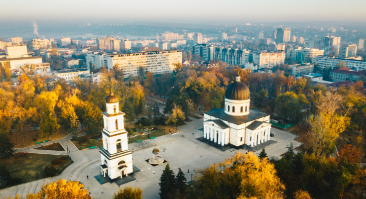 Drohnenaufnahme des Kathedralparks in Chișinău mit der weiß-klassizistischen Kathedrale mit schwarzer Kuppel und freistehendem Glockenturm, umgeben von herbstlichen Bäumen und Stadtbebauung.