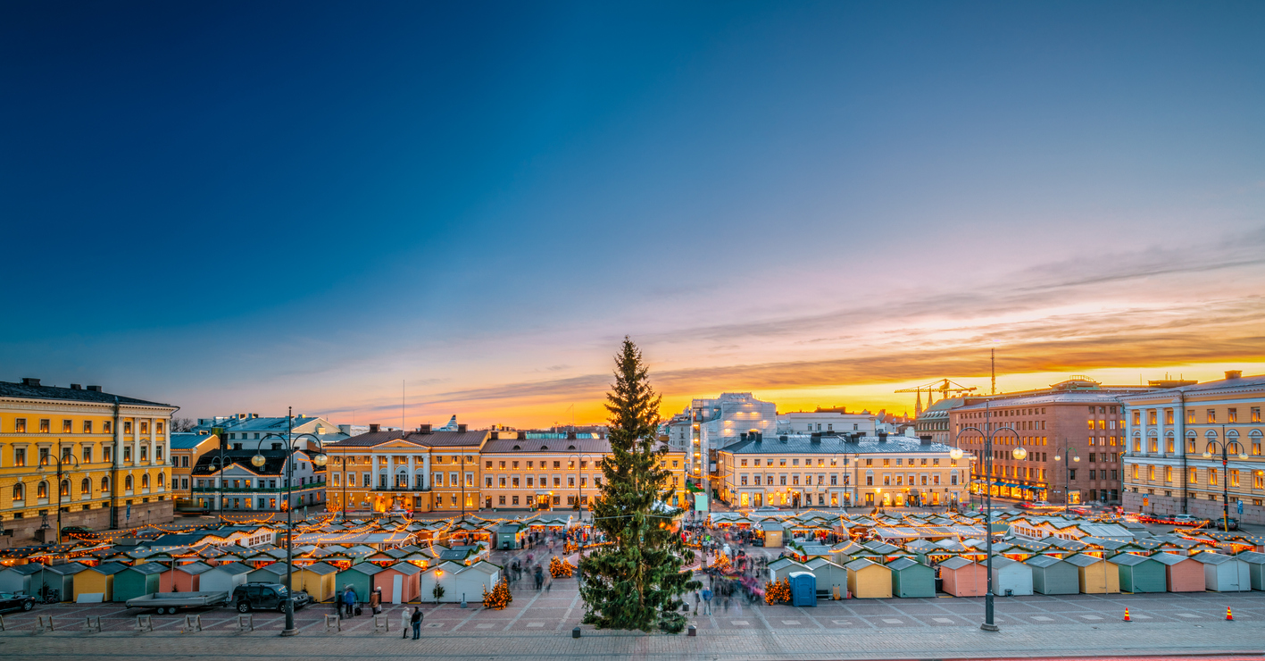 Weihnachtsmarkt in Helsinki bei Sonnenuntergang mit beleuchtetem Tannenbaum und Marktständen.