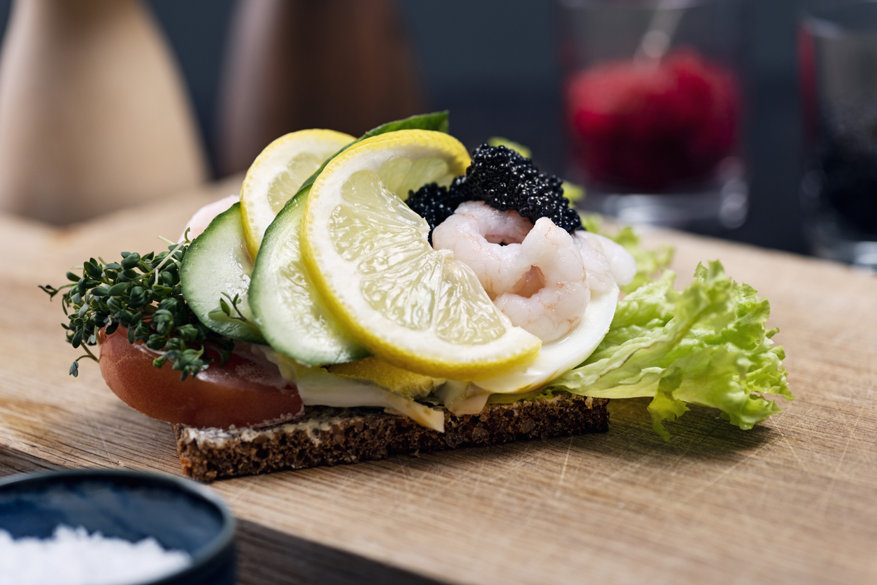 Nahaufnahme eines dänischen Smørrebrøds mit Roggenbrot, Garnelen, Ei, Zitrone, Gurke und Kaviar.