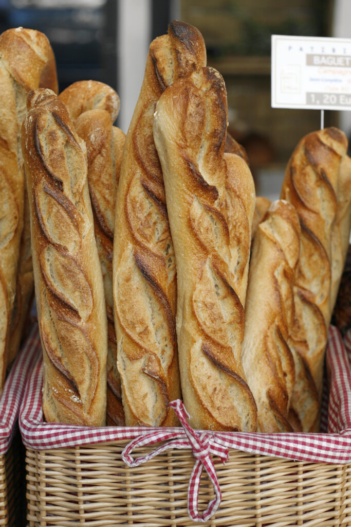 Frisch gebackene französische Baguettes in einem Weidenkorb mit rot-weiß kariertem Stoffeinsatz, goldbraun gebacken und knusprig.
