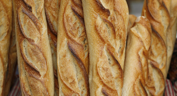 Frisch gebackene französische Baguettes in einem Weidenkorb mit rot-weiß kariertem Stoffeinsatz, goldbraun gebacken und knusprig.