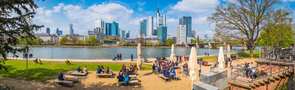 Menschen genießen das sonnige Wetter am Mainufer in Frankfurt mit Blick auf die Skyline.