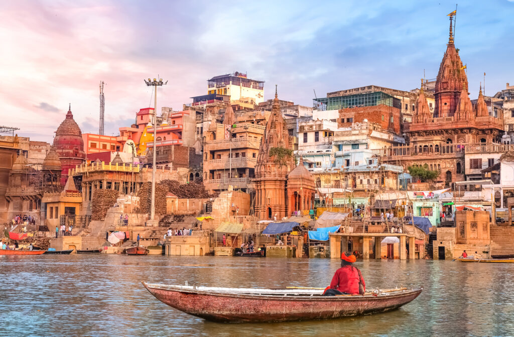 Blick auf die bunten Ghats von Varanasi am Ganges mit Boot und Tempeln im Hintergrund.