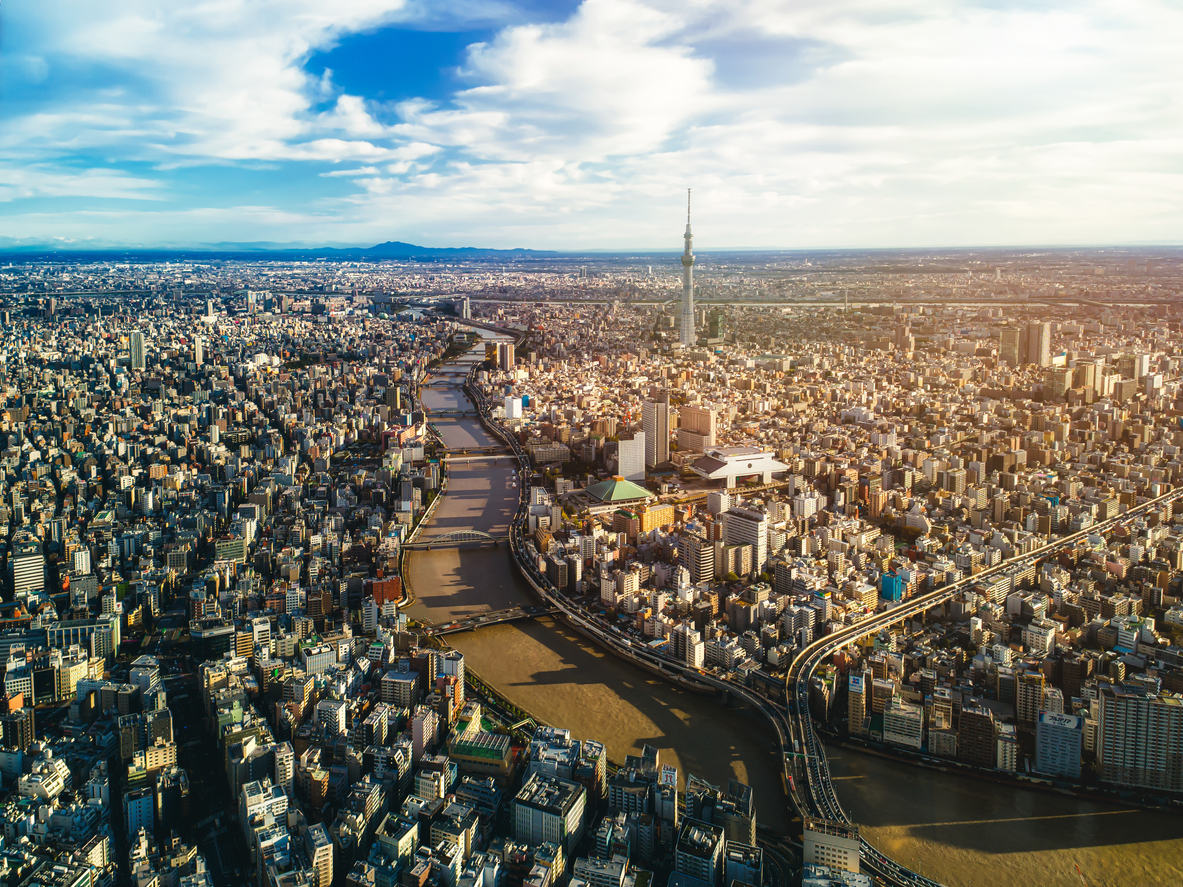 Luftaufnahme von Tokio, Japan, mit dicht bebauten Hochhäusern, dem Fluss Sumida, mehreren Brücken und dem markanten Tokyo Skytree im Hintergrund.