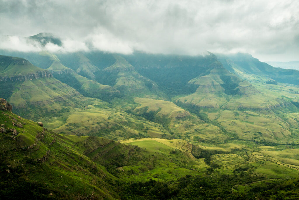 Nebelverhangene, grüne Berglandschaft der Drakensberge mit sanften Tälern und wolkenverdeckten Gipfeln.