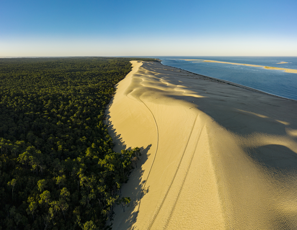 Luftaufnahme der Dune du Pilat in Frankreich, die größte Wanderdüne Europas, mit goldenem Sand, angrenzendem Pinienwald und Blick auf den Atlantik.