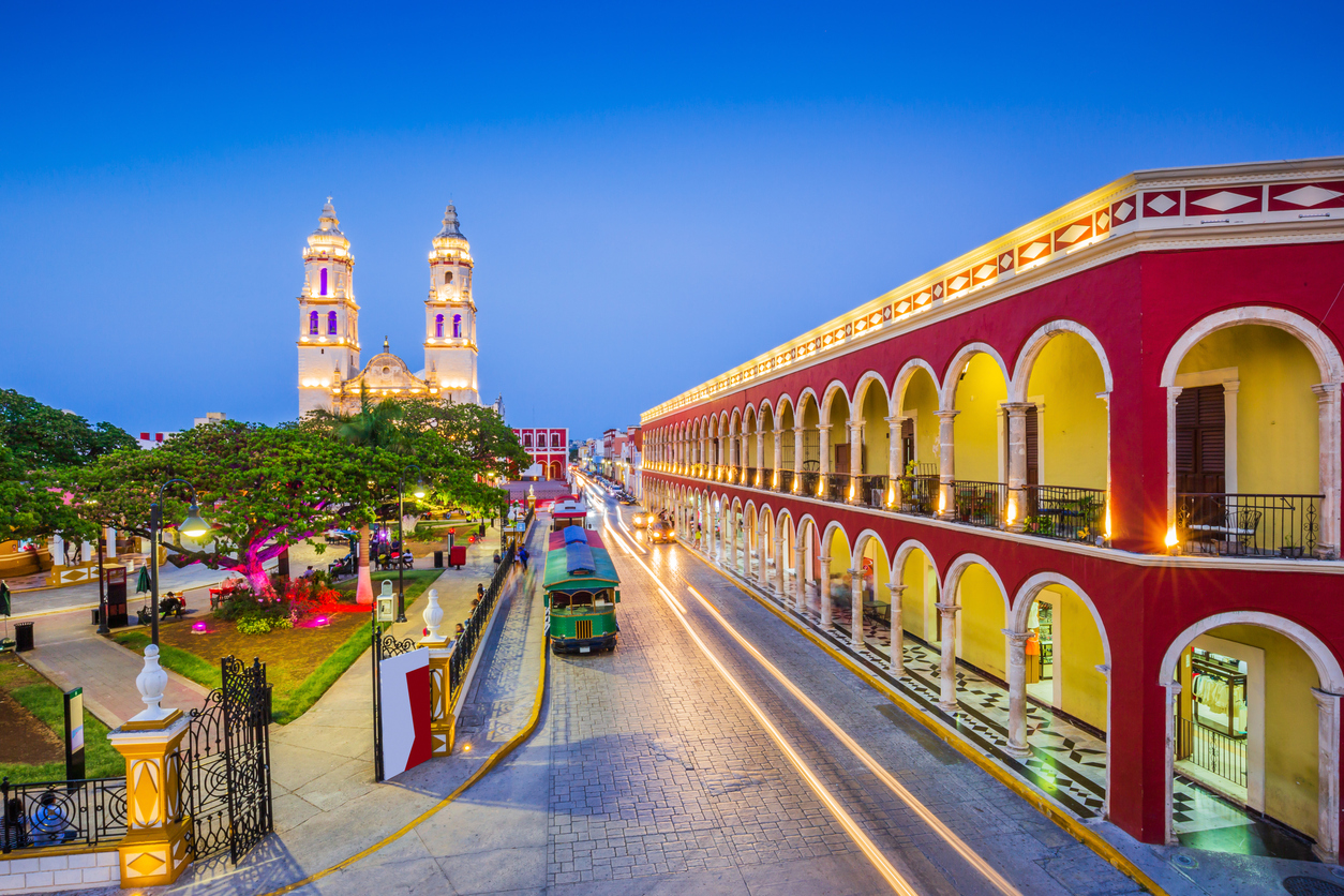 Abendaufnahme: Kathedrale von Campeche mit zwei Türmen, rote Arkadenfassade am Parque Principal, Lichtspuren.