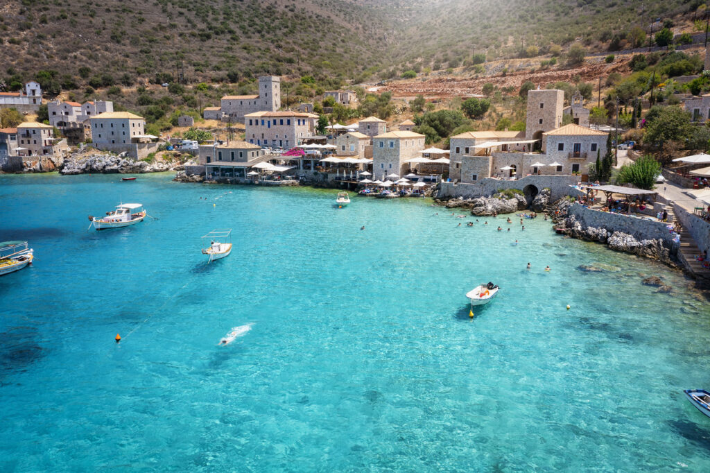 Steinernes Küstendorf auf der Peloponnes (Mani) an einer türkisfarbenen Bucht mit Booten und Badenden