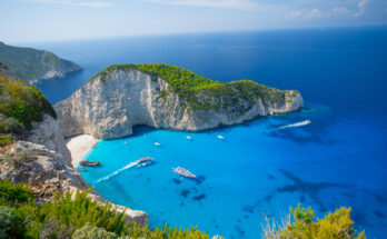 Türkisfarbene Bucht auf Zakynthos mit weißen Klippen, Sandstrand und Booten aus der Vogelperspektive.