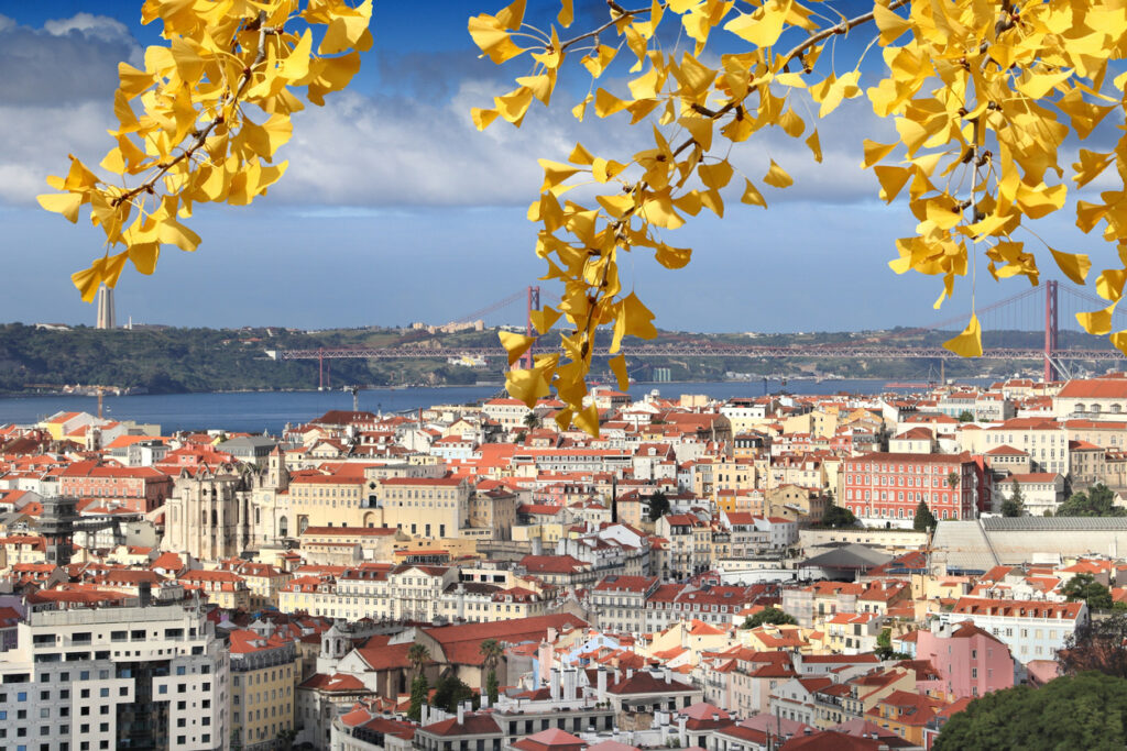 Lissabon mit roten Dächern, Ponte 25 de Abril und Cristo-Rei, eingerahmt von gelben Herbstblättern.