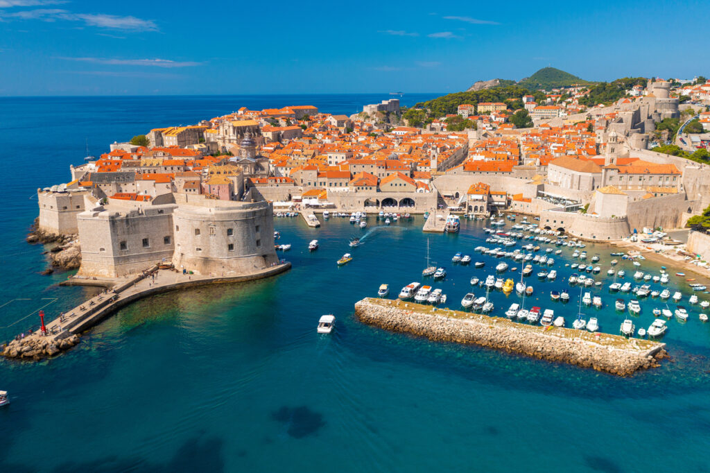 Luftaufnahme von Dubrovniks Altstadt mit Festungsmauern und Yachthafen im türkisblauen Meer.