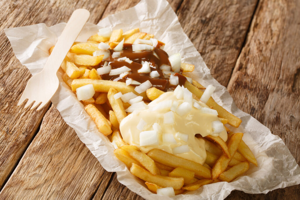 Niederländisches Patatje Oorlog, Pommes mit Mayonnaise, Erdnusssauce und gehackten Zwiebeln, serviert in Papier.