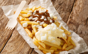 Niederländisches Patatje Oorlog, Pommes mit Mayonnaise, Erdnusssauce und gehackten Zwiebeln, serviert in Papier.