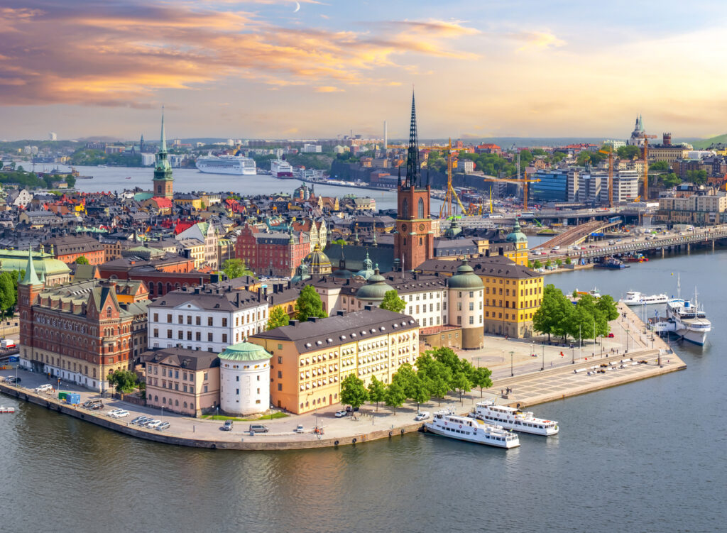 Stockholm, Panorama der Altstadtinsel Riddarholmen mit der Riddarholmskyrkan, farbige Fassaden, Ausflugsboote am Kai, ruhiges Wasser, warmer Abendhimmel