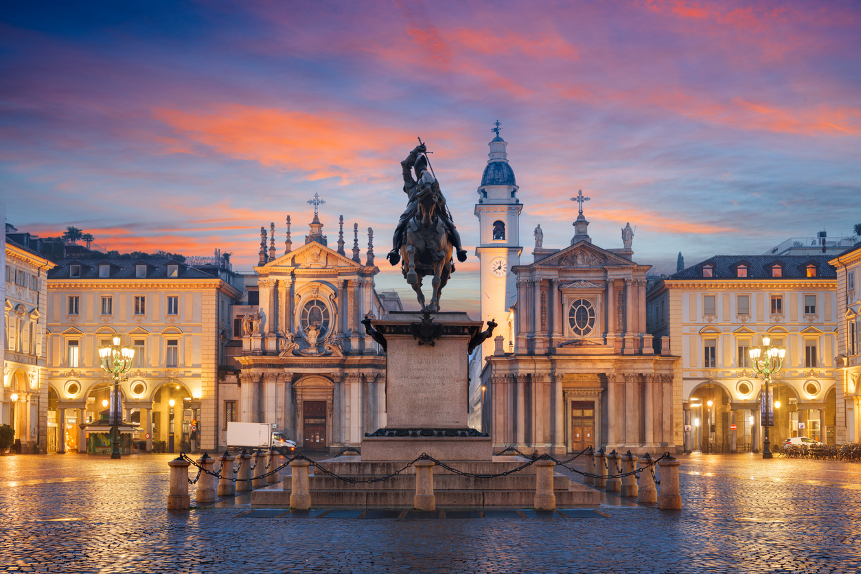 Abend-/Morgenstimmung auf der Piazza San Carlo in Turin mit der Reiterstatue Emanuele Filiberto vor den barocken Kirchen Santa Cristina und San Carlo Borromeo, rosa-blauem Himmel und nassen Pflastersteinen.