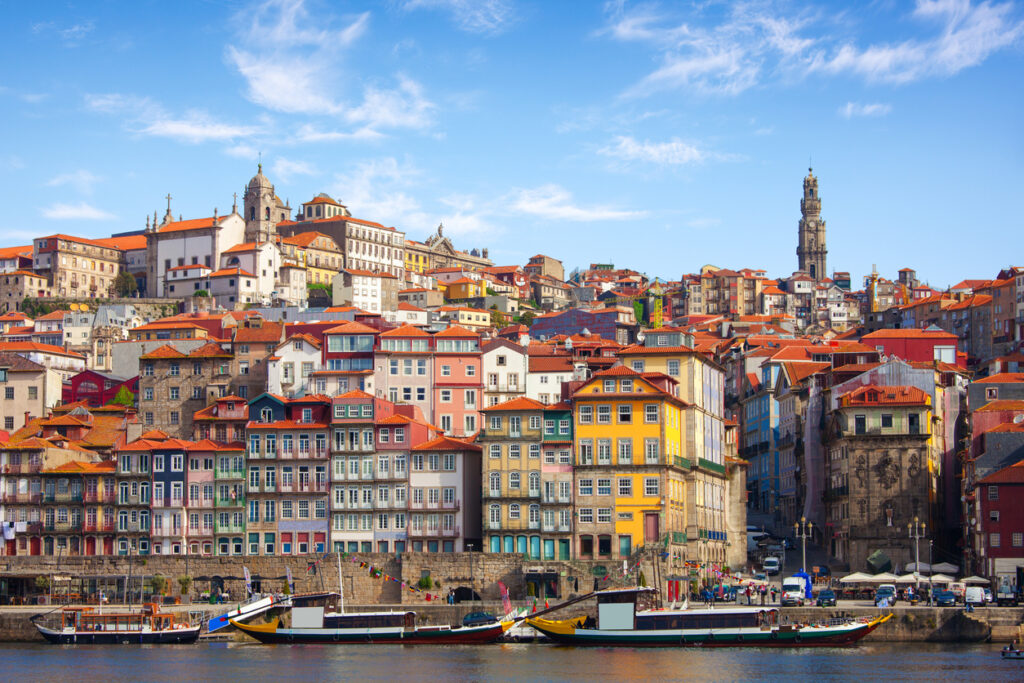 Bunte Altstadthäuser der Ribeira in Porto mit Rabelo-Booten und Clérigos-Turm am Douro.