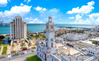 Weißer Uhrturm und Verwaltungsgebäude am Hafen von Veracruz; Meer und blauer Himmel mit Wolken.