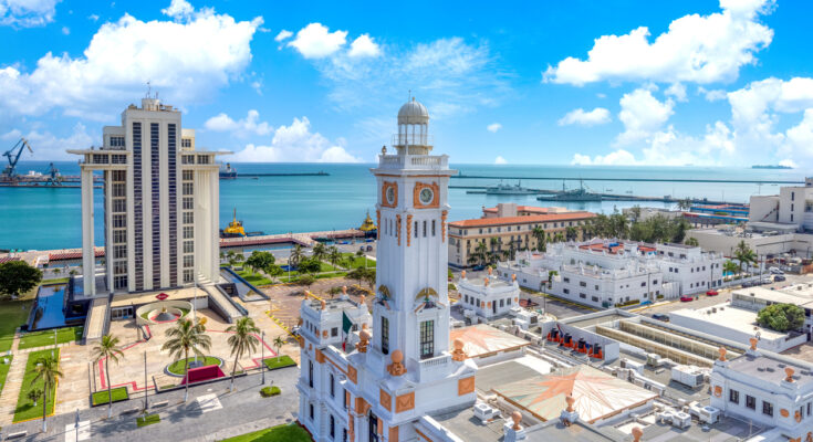 Weißer Uhrturm und Verwaltungsgebäude am Hafen von Veracruz; Meer und blauer Himmel mit Wolken.