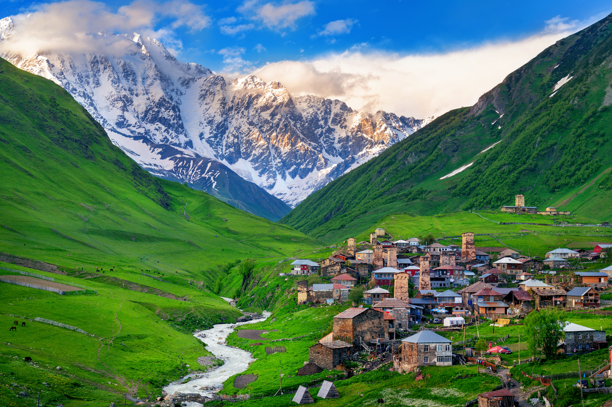Dorf Ushguli in Swanetien mit Svan-Wehrtürmen, grünem Tal und schneebedecktem Schchara-Massiv im Hintergrund.